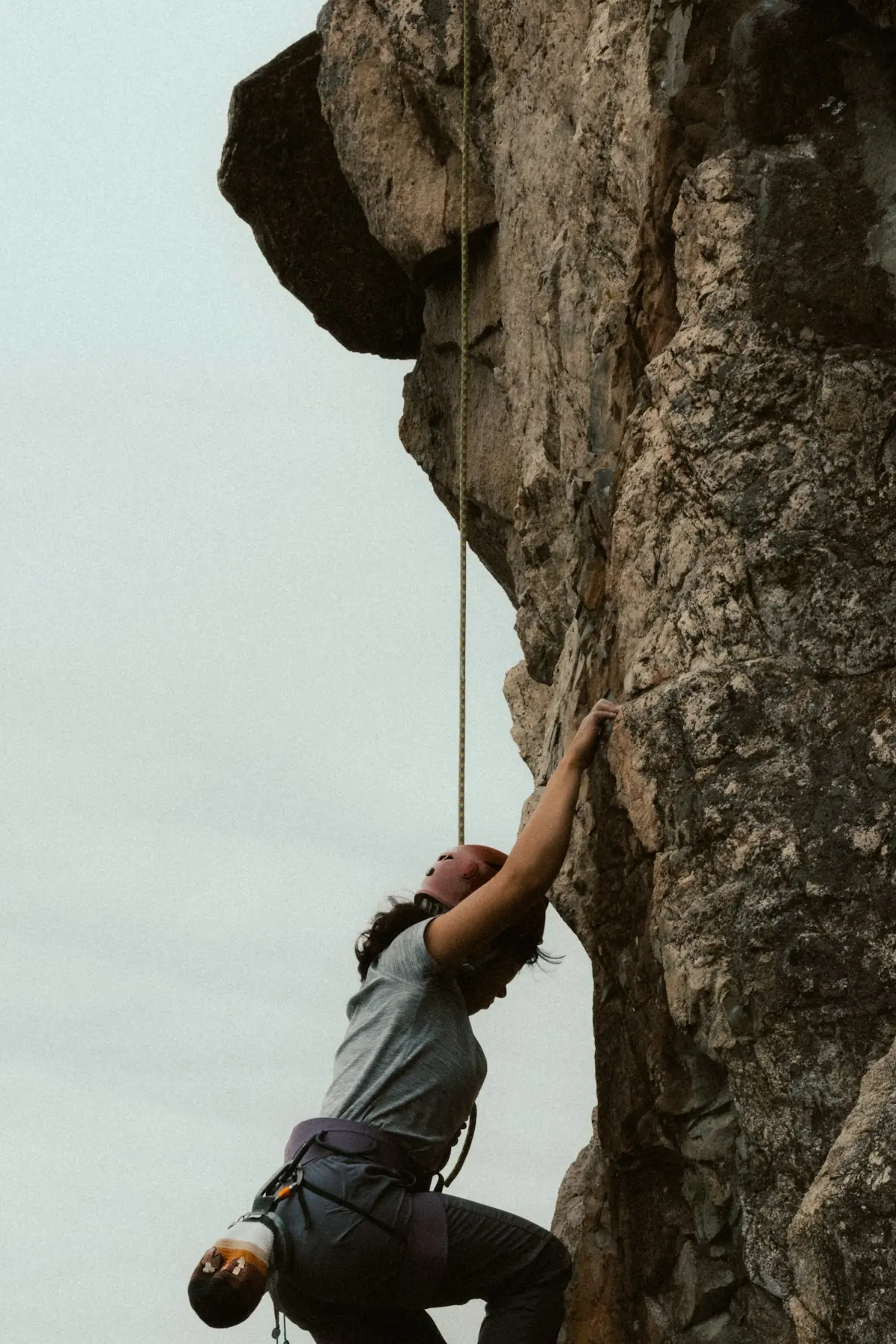 A roped climber working up a steep, sunlit rock face.